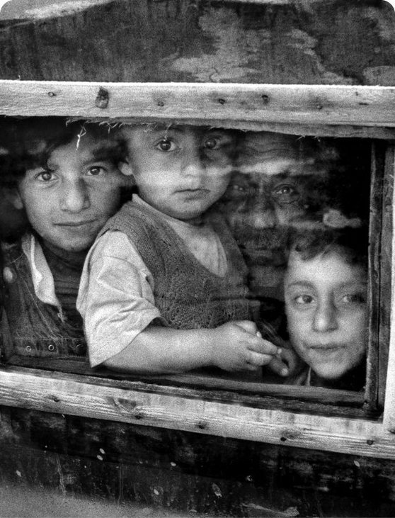 Three children looking through a wooden window, black and white